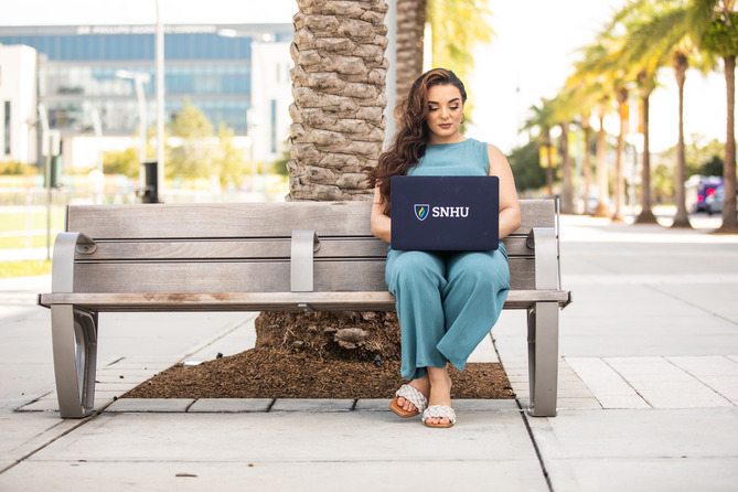 a SNHU student sitting on a bench working on her laptop